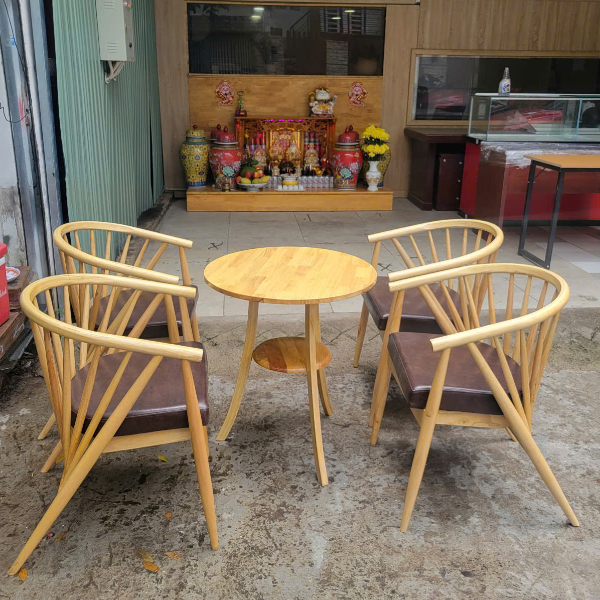 Bộ bàn ghế cafe gỗ mới: 1 bàn tròn gỗ có kệ và 4 ghế tựa nệm da nâu, bố trí ngoài sân